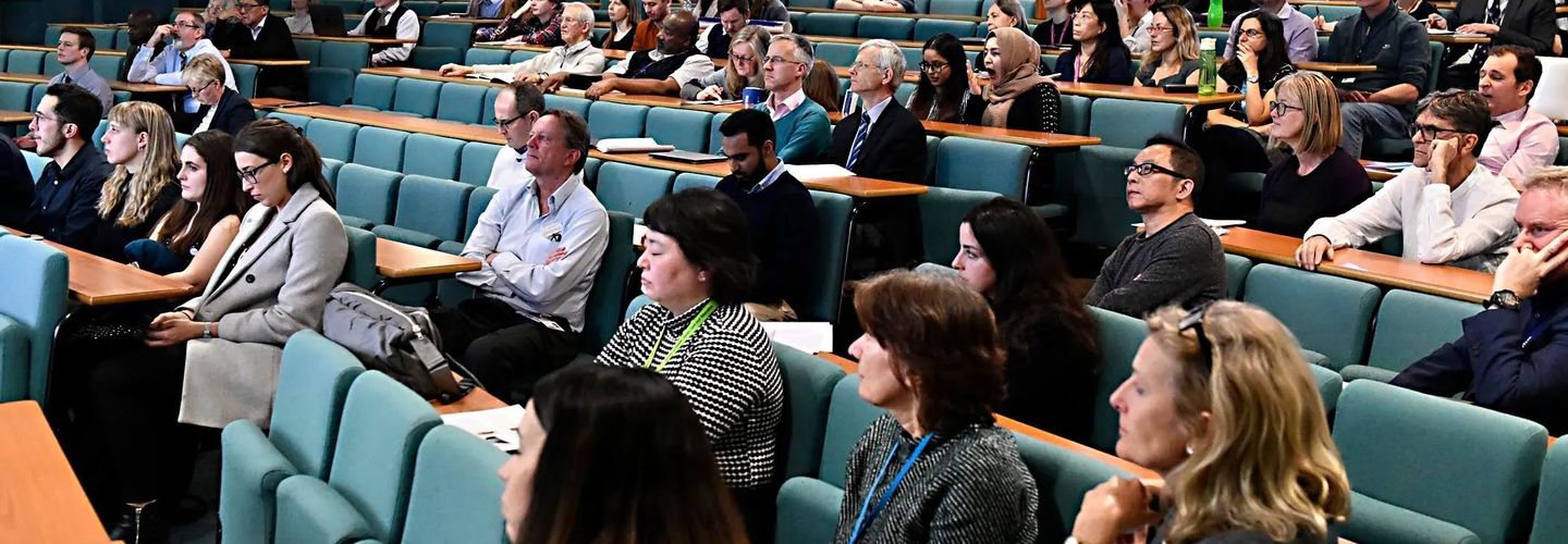 A crowded lecture hall filled with people, all focused on a presentation being delivered at the front of the room.