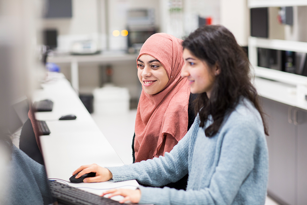 Two students sitting together looking at a computer screen smiling