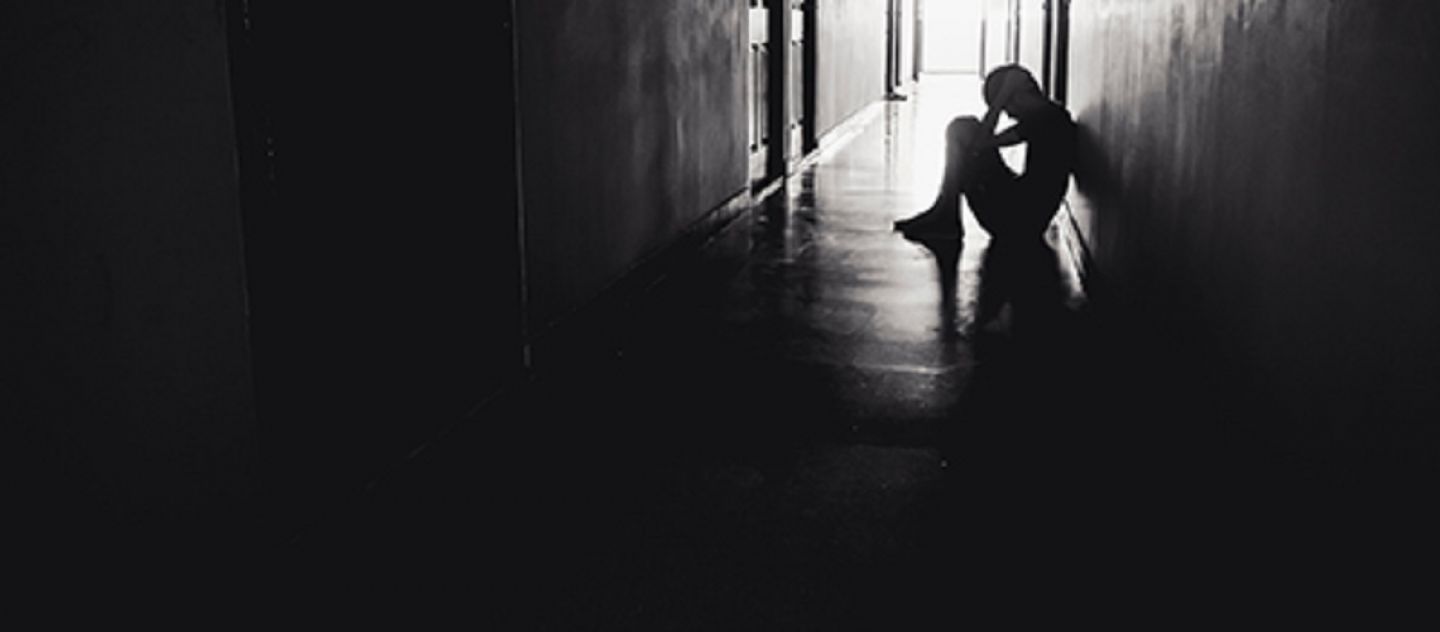 black and white silhouette of a sad person sitting in a corridor with head in hands