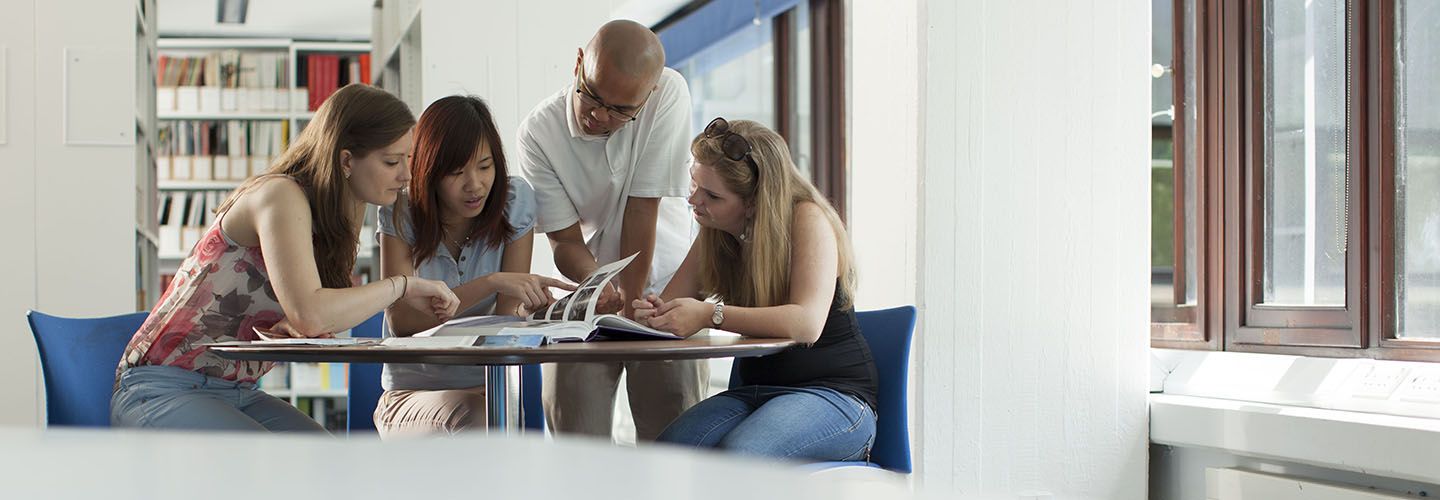 Diverse group of students studying a book together at a table in the library.