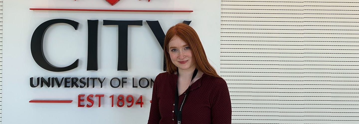 Jenna Martin-Zahid, third year Optometry student at City, standing in front of the university logo
