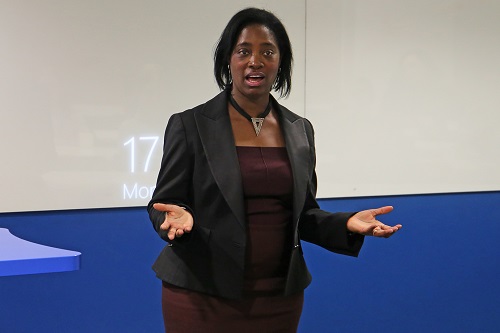 Associate Dean, Michelle Ellis speaking to an audience with hands raised by ears, asking a question