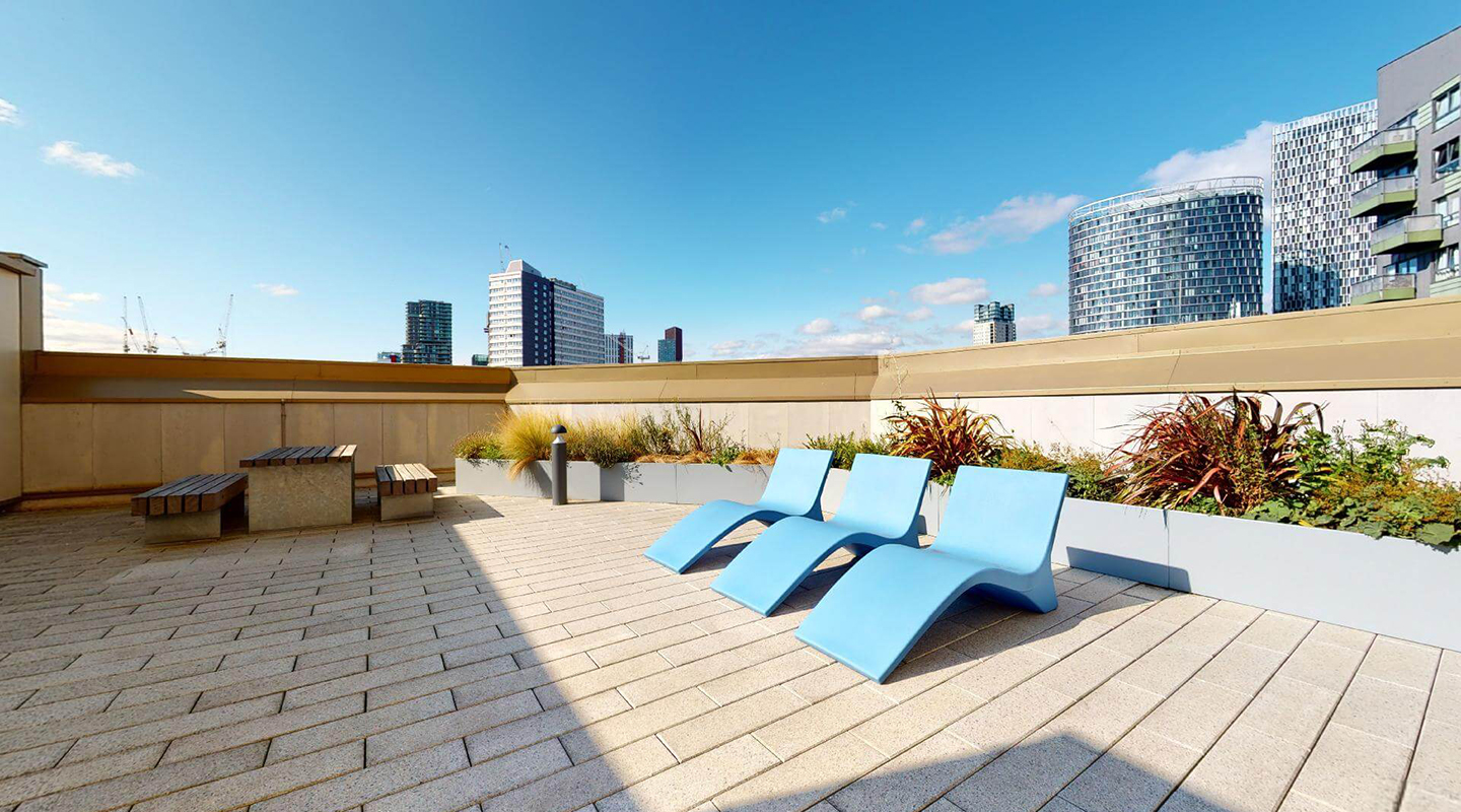 Paved communal roof garden with raised planters,  tables and loungers.
