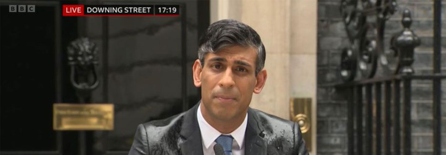 An image of PM Rishi Sunak standing in front of podium in front of Downing Street calling an election, in the rain.