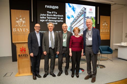 Four men and a woman on stage in a line in front of a screen with the Bayes logo