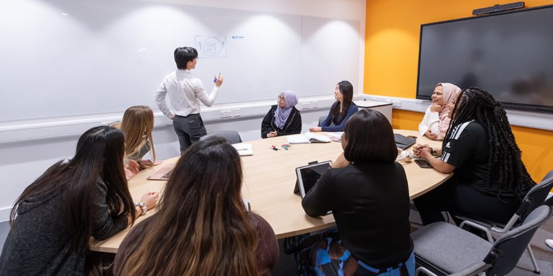Students working together in base room sat round table in front of digital screen