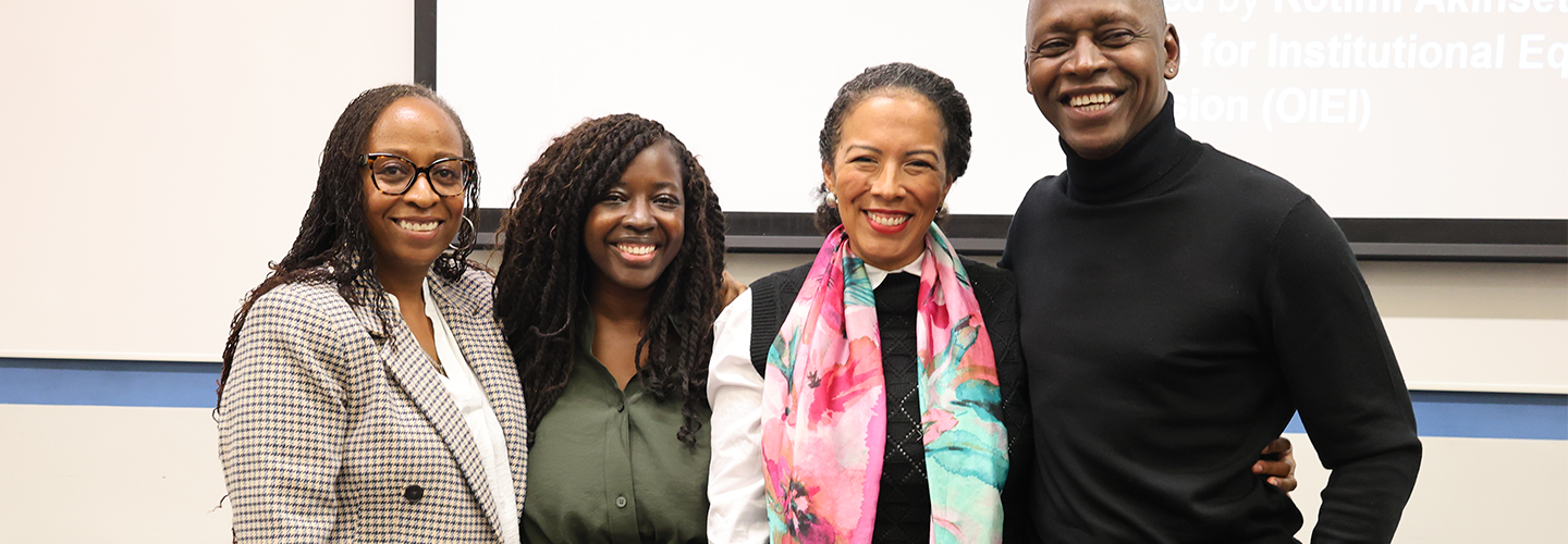 Three women and one man stand together smiling