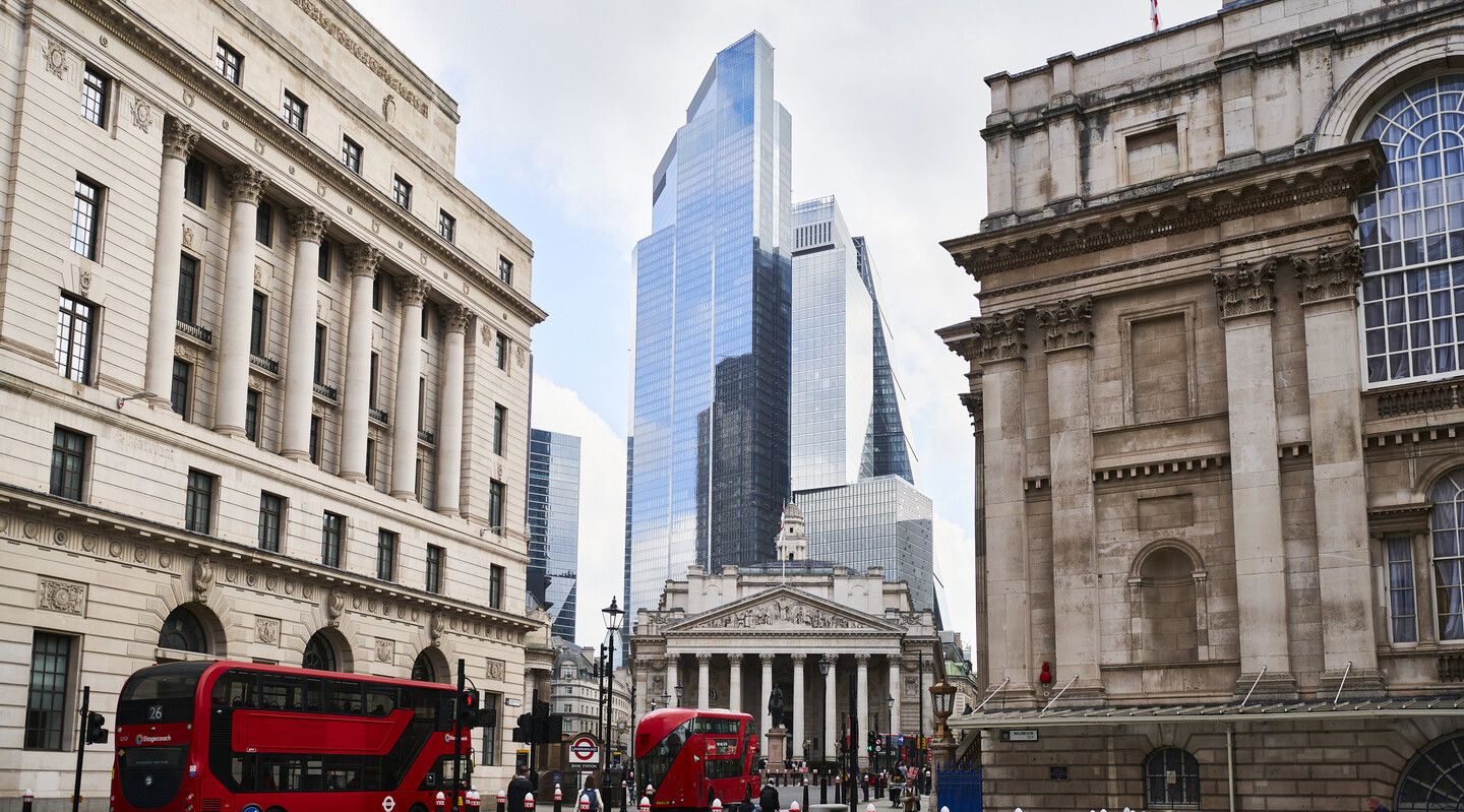 Red london busses amongst skyscrapers and old buildings including the bank of England
