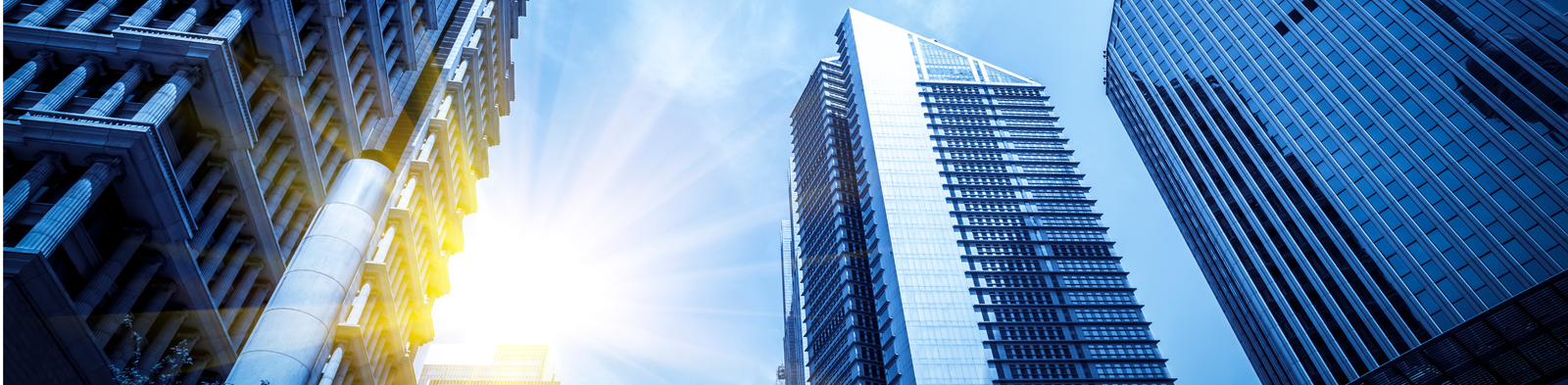 looking up at tall buildings with the sun in the sky