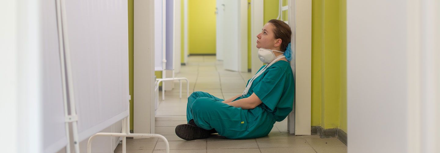 Covid nurse sitting on the floor looking tired and thoughtful