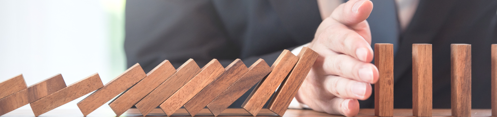 A hand prevents a stack of dominoes from falling