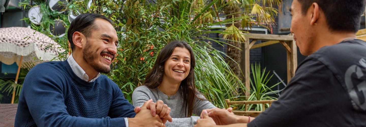 Students sitting at a table, smiling and chatting to each other