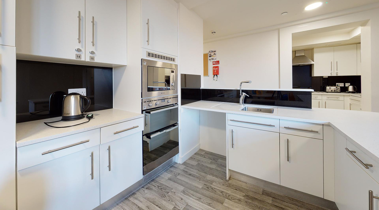 Shared kitchen with built in oven and grill, cupboards (upper ones numbered) sink and kettle.
