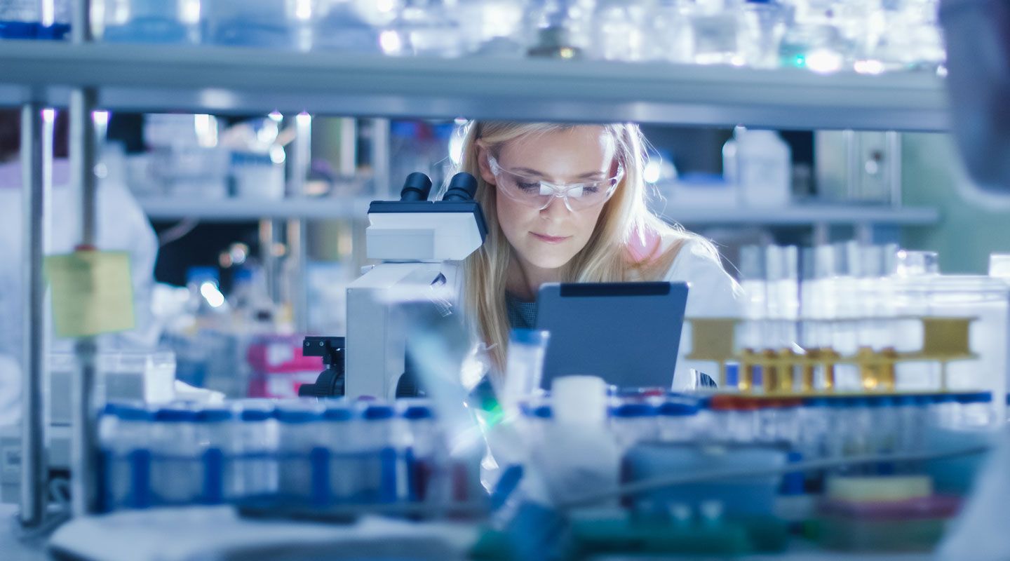 Research Female Scientist is using a Microscope and a Tablet Computer while Working in a Modern Laboratory. Doing Genetic and Pharmaceutical Research