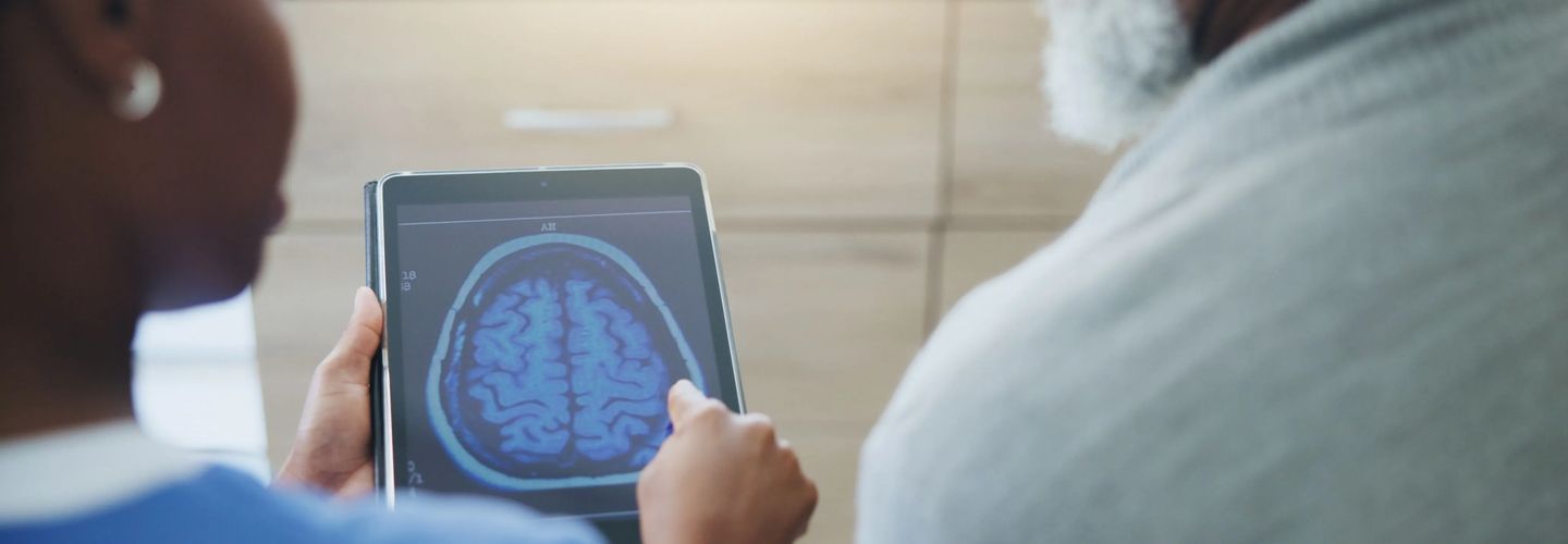Doctor using tablet to show brain scan to elderly man for medical diagnosis in healthcare setting.
