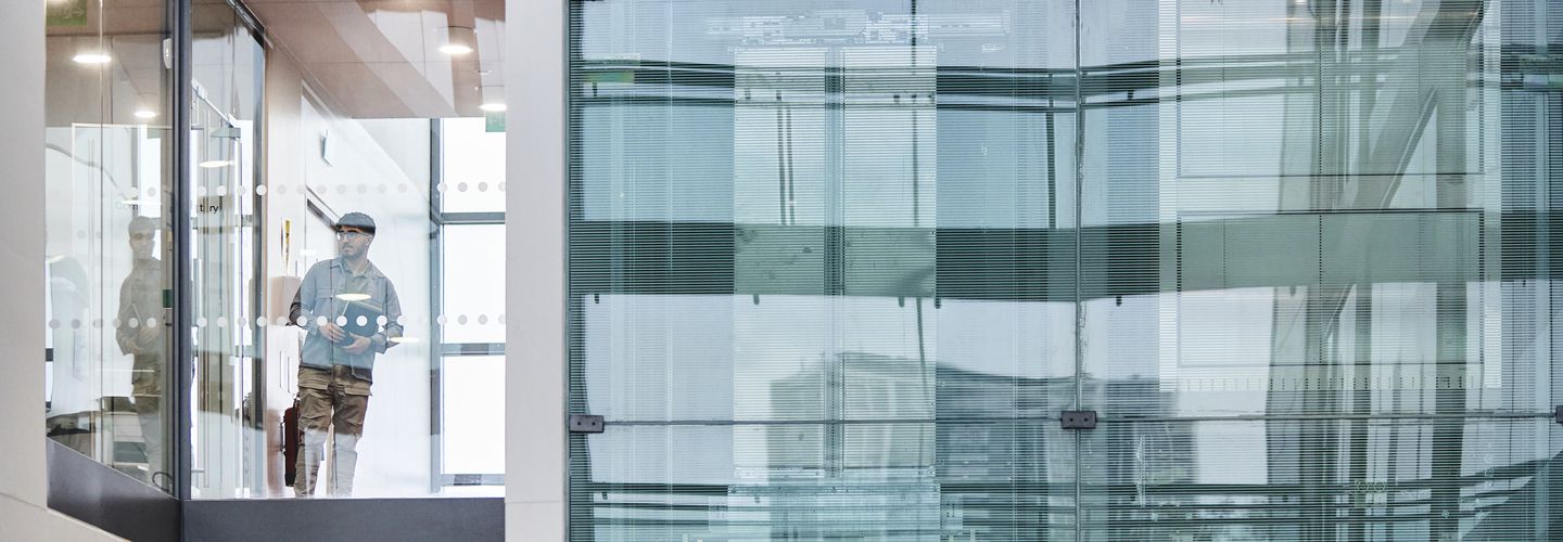 A man walks through a modern glass corridor inside the Rhind Building