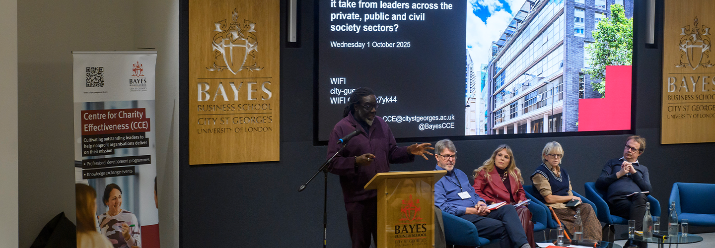 A man talks at a lectern and four people seated to his left listen.
