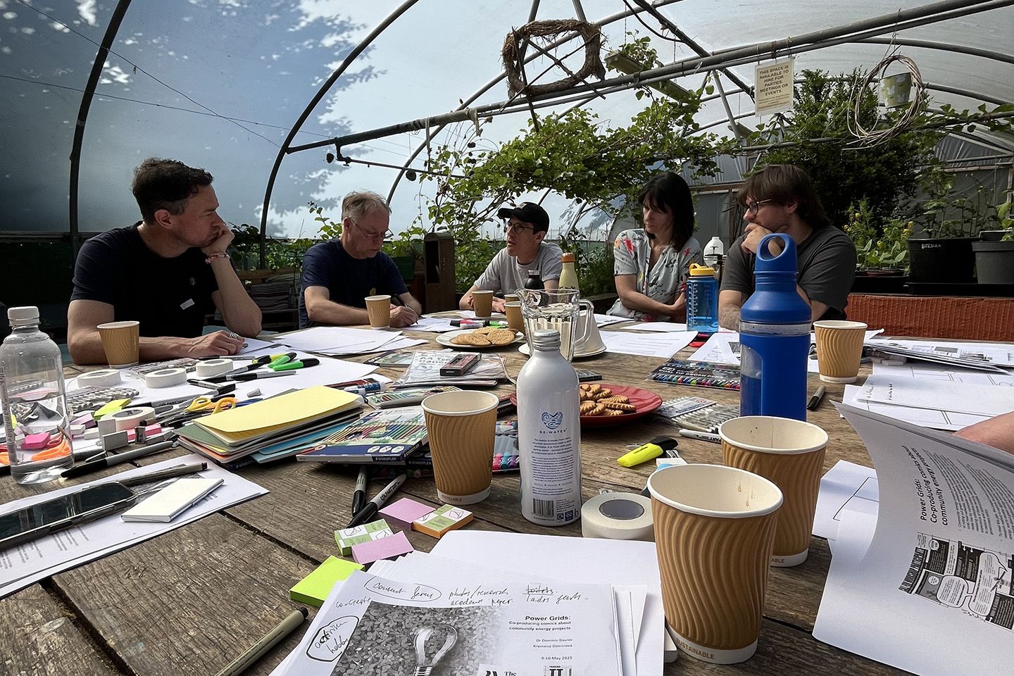 People with zine making materials at a table in a greenhouse