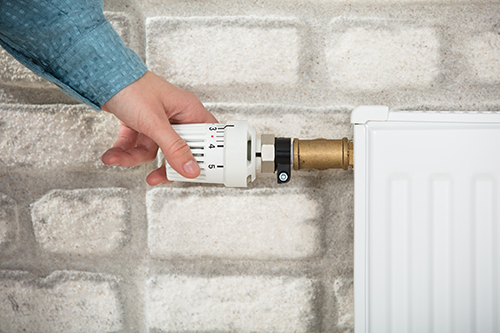 A hand turns the handle on a radiator