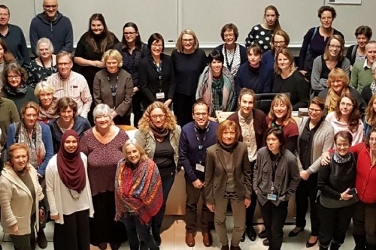 Collaboration of Aphasia Trialists (CATs) group photo of many international members looking up at the camera from a lower level