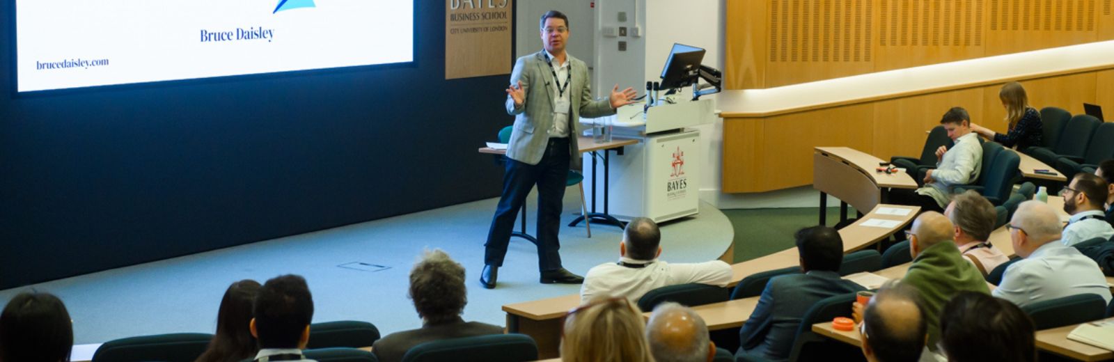 Professor Andre Spicer walks around the stage as he gives the welcome to the alumni forum