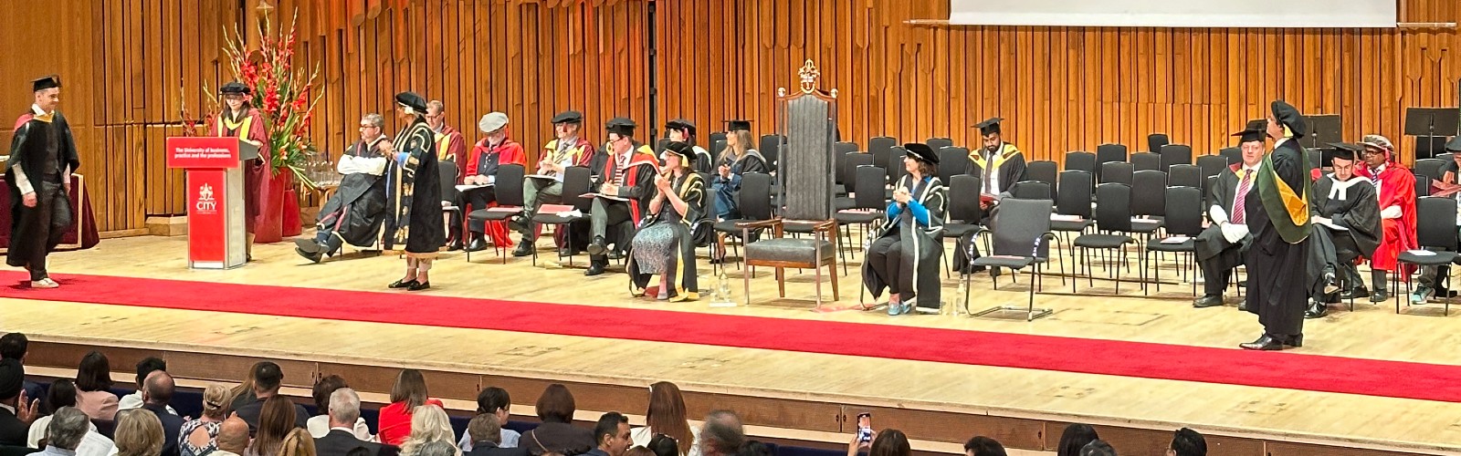 The School Dean and other leaders and guests sit on the stage during the ceremony