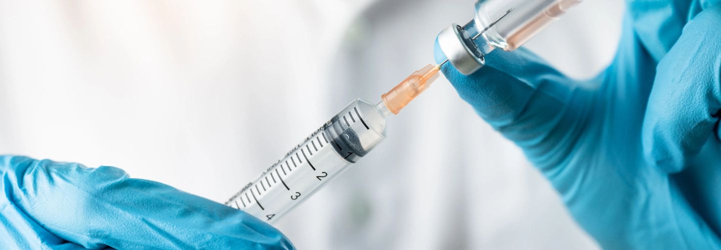 A nurse with blue gloves holding a vaccination shot