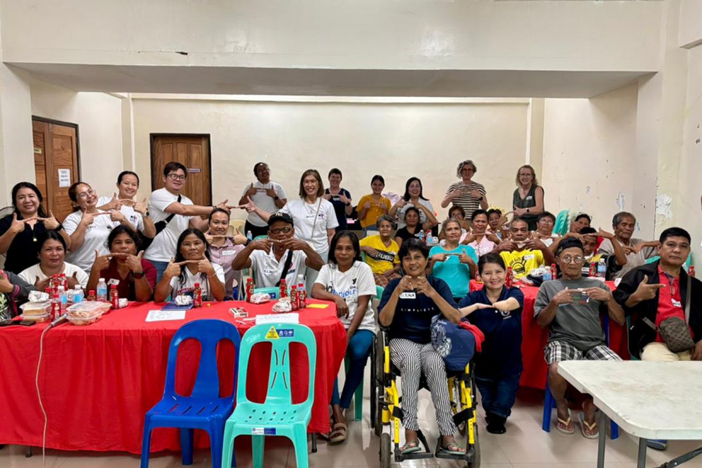 The image shows a Philippine community of stroke survivors, carers and Barangay health workers taking part in a co-design event. They are all making the sign for 