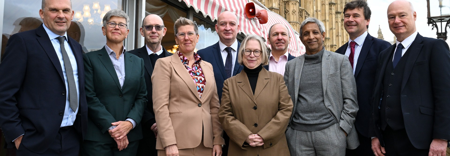 A group of people dressed in suits stand in front of Parliament for a posed photo