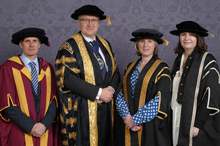 Two men and two women pose wearing doctoral bonnets 