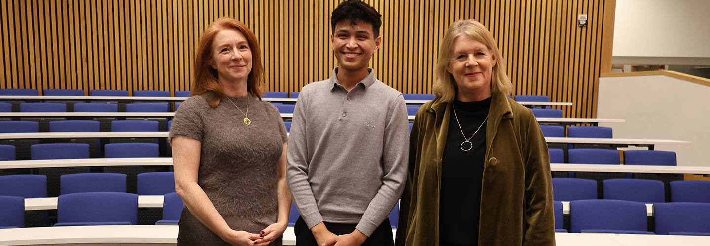 Three people pose for a photo in a lecture hall
