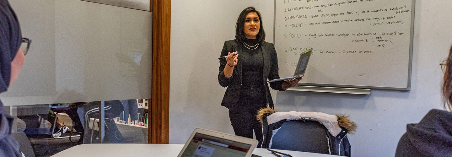 Female student discusses key points on a whiteboard with two other female students