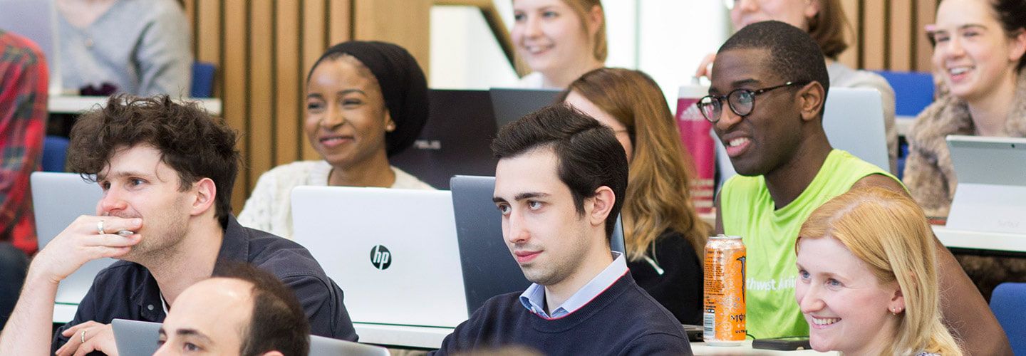 Students smiling using laptop in a lecture room