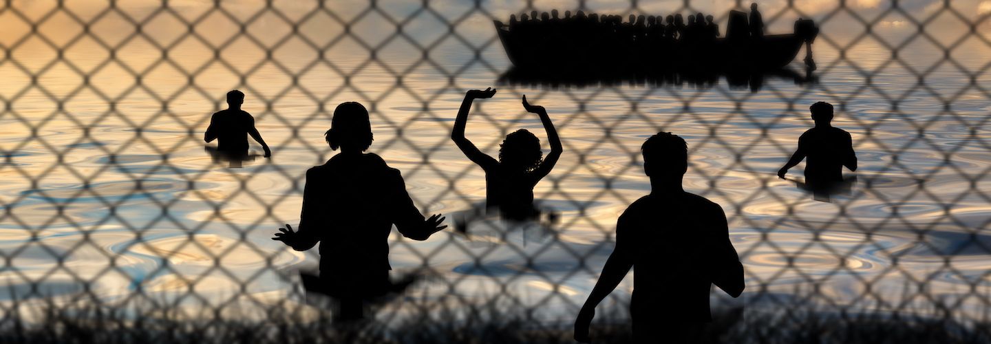 Refugees swim to shore against the backdrop of a chain wire fence