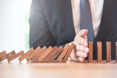 A hand prevents a domino pile from falling