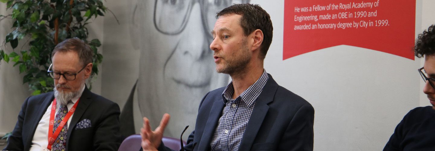 Male academic sitting on a panel speaking to a group of people.