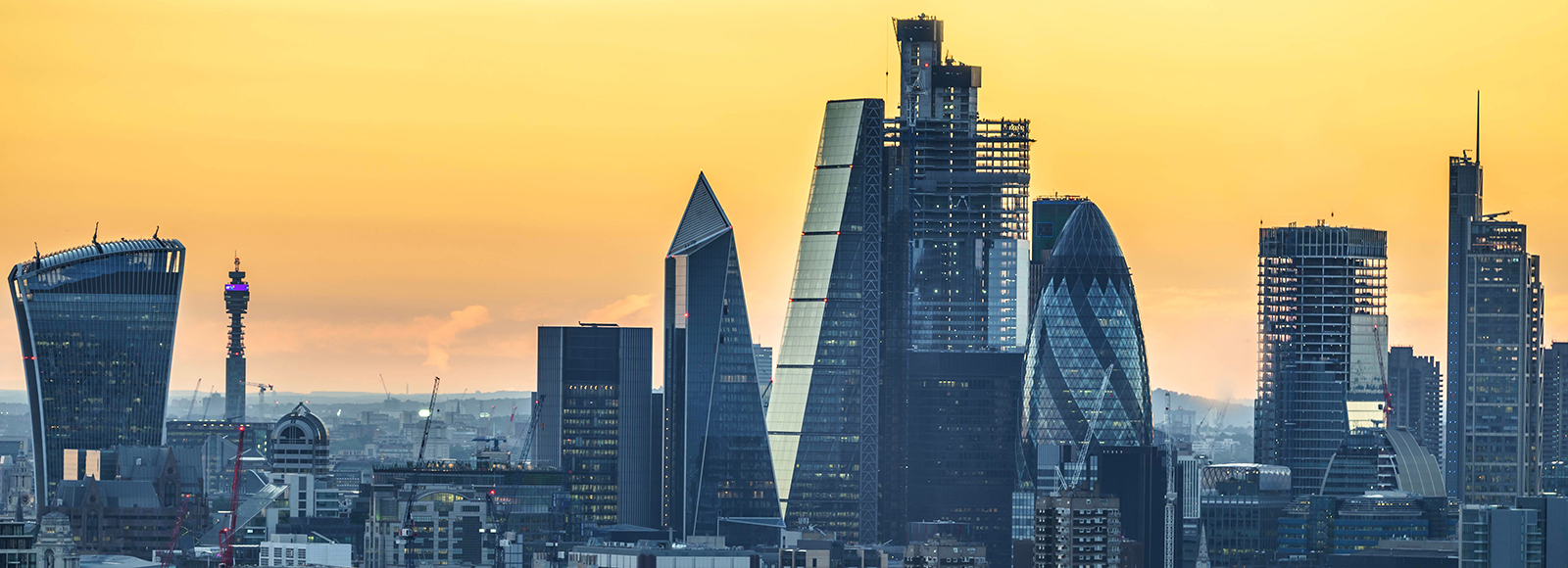 Grey buildings of the City of London sit against a yellow and orange sky. Buildings include Cheese Grater, Gherkin and Walkie Talkie amongst many others.