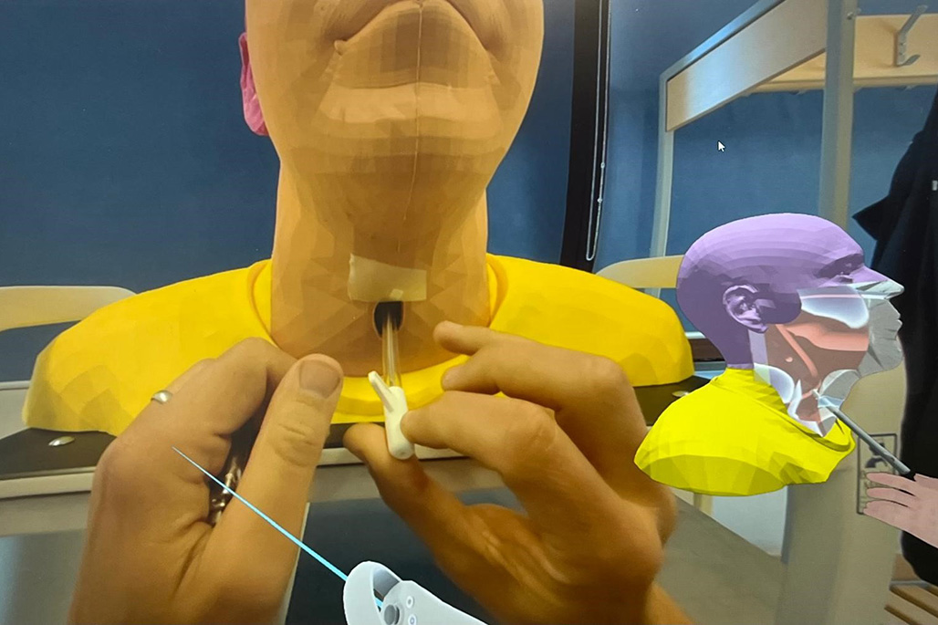 A post-registration healthcare professional learner inserting a voice prosthesis brush into a voice prosthesis within a 3D printed model's trachea. They are following audio-visual instructions that walk them through the procedure via a VR headset.
