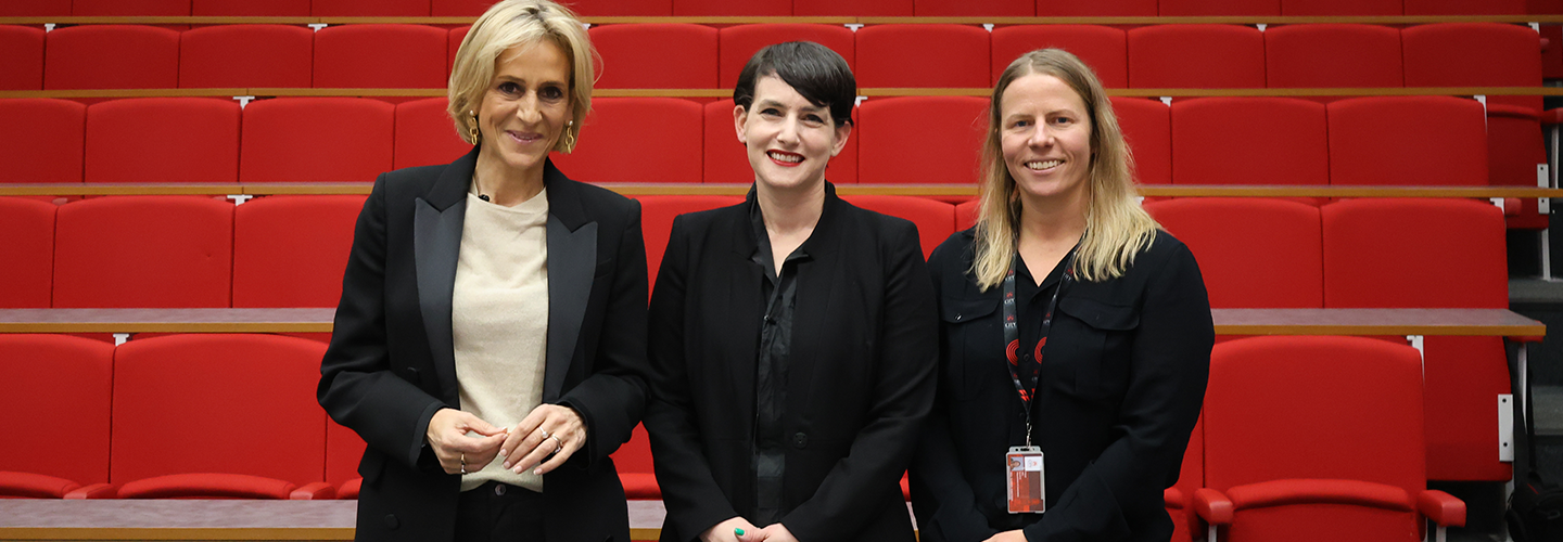 Three women wearing professional clothing pose for a photo in a lecture hall, with red seats behind them 
