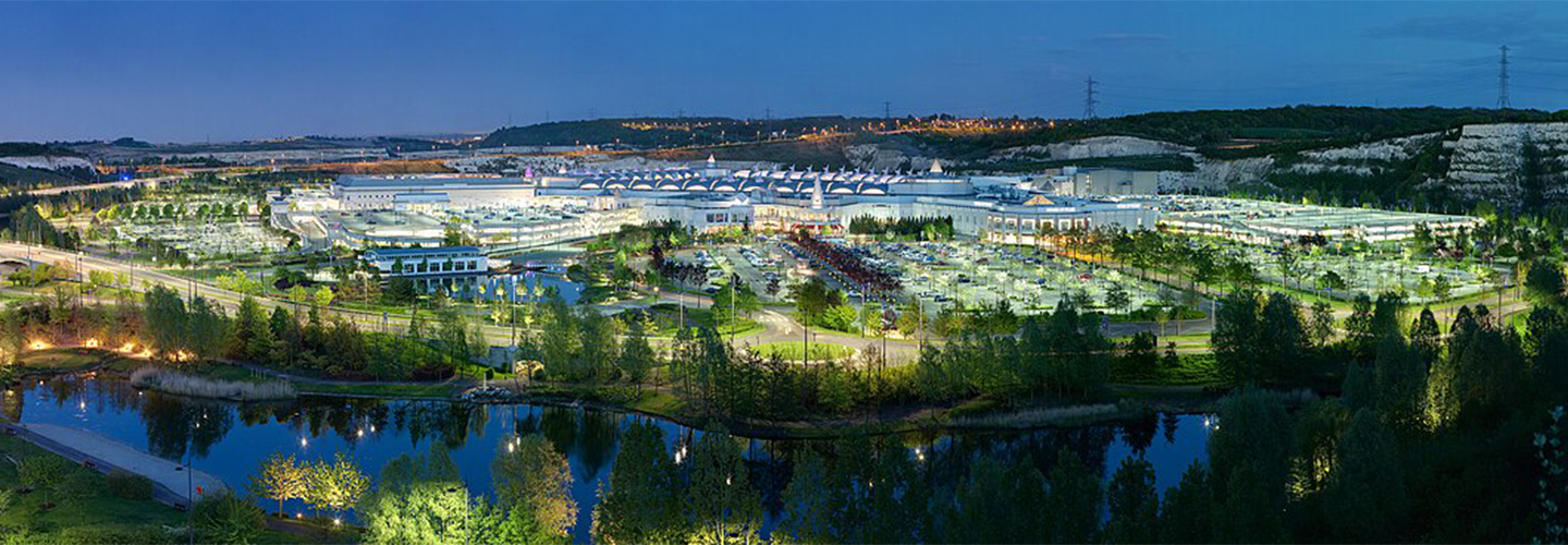 The lights of a shopping centre from afar with a stream running past it