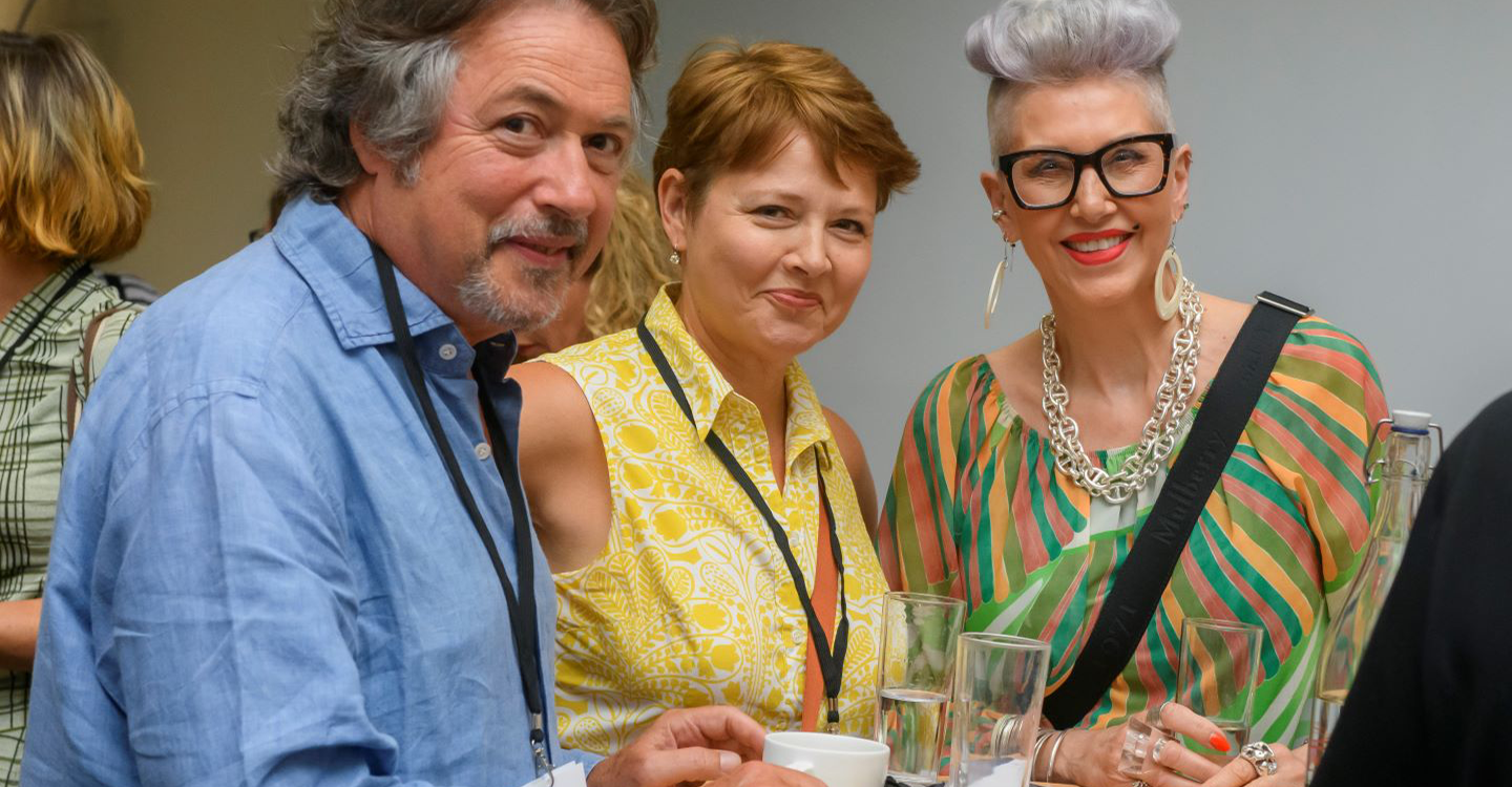 Two women and a man stand at a small table.