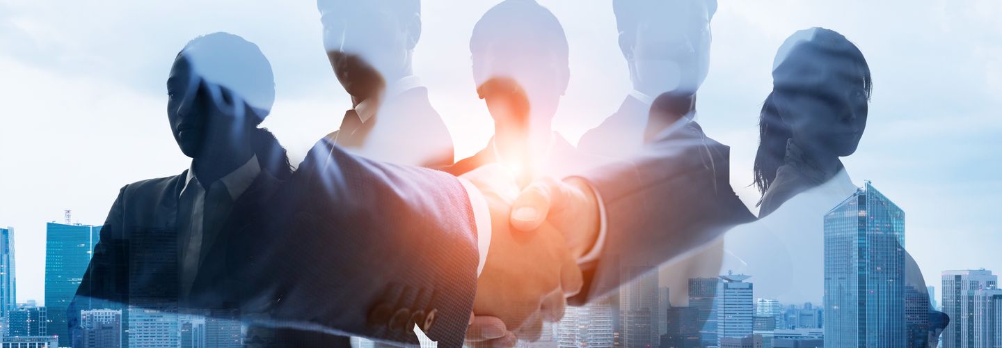 Businessmen shaking hands overlay on men and women wearing suits, over a background of city office buildings.