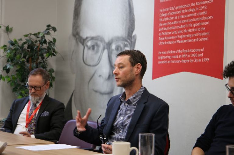 Male academic sitting on a panel speaking to a group of people.