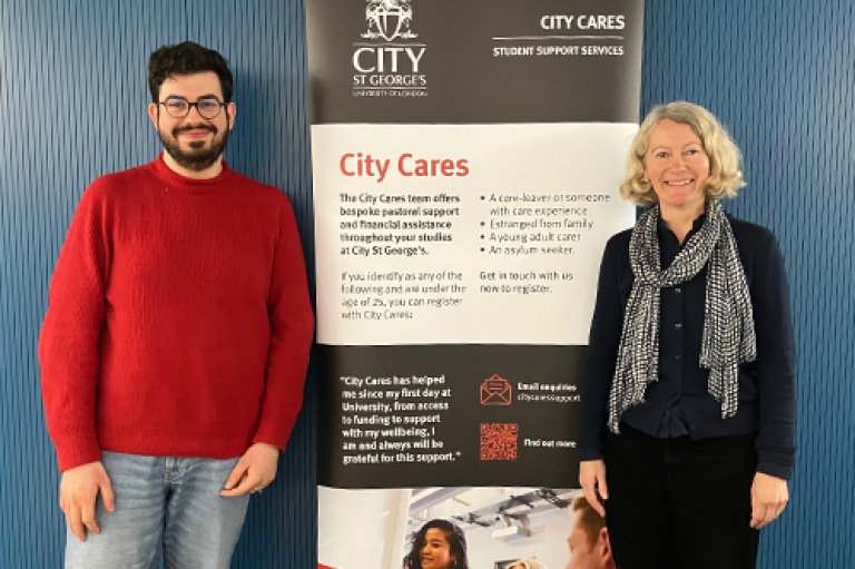 Two members of staff stand with a City Cares banner in front of a blue wall