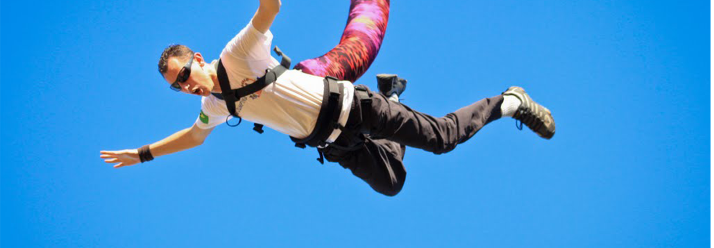 A bunjee jumper has their arms stretched out as they fall while attached to a thick colourful rope