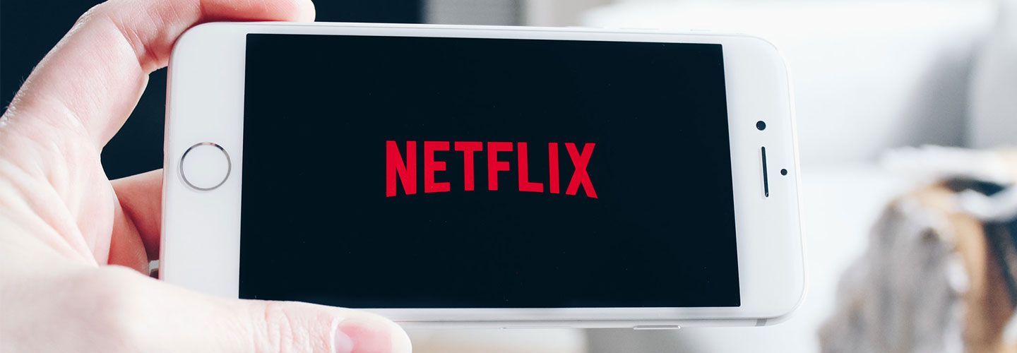 A hand holds up a smartphone with the screen open to the Netflix homepage (a black screen with the red NETFLIX logo)