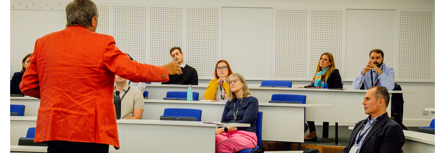 A from behind view of Professor Stephen Thomas in a bright jacket with his hand in the air as five people listen