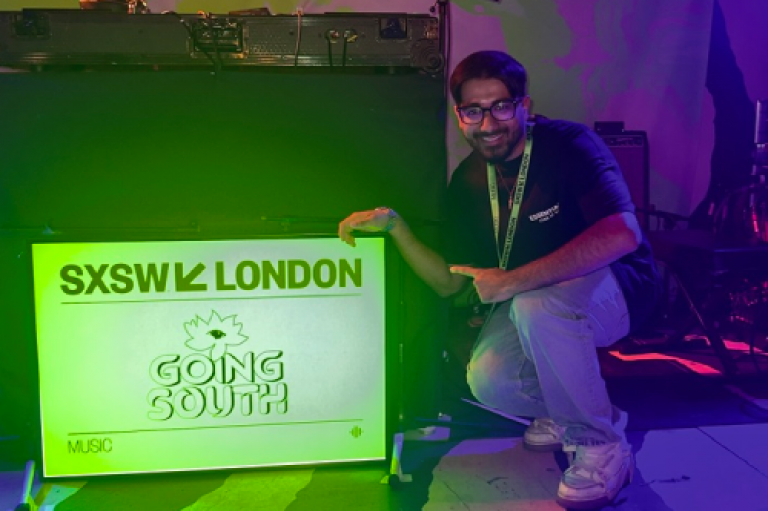 Rohit Sands is crouching and pointing at a sign that says 'SXSW London Going South'.