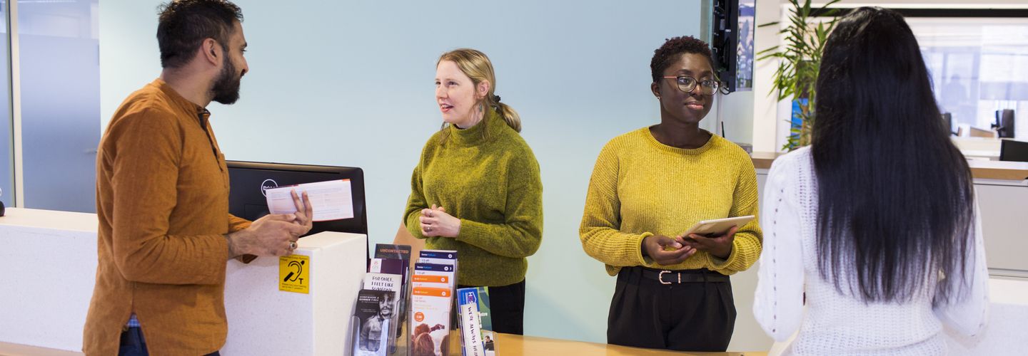 Students and support services staff talking across a service counter.