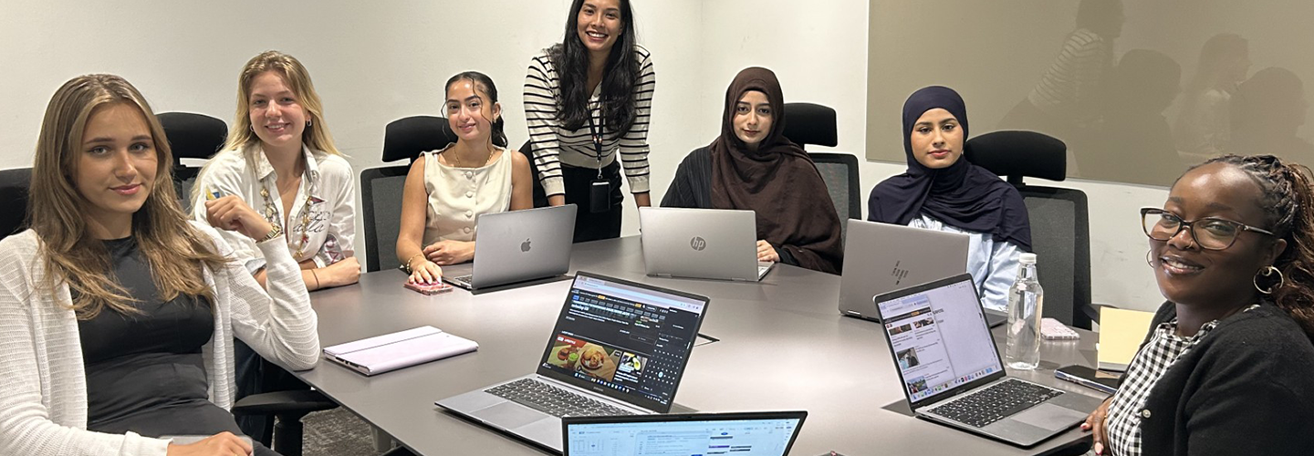 A group of women with laptop sit at a table in a boardroom